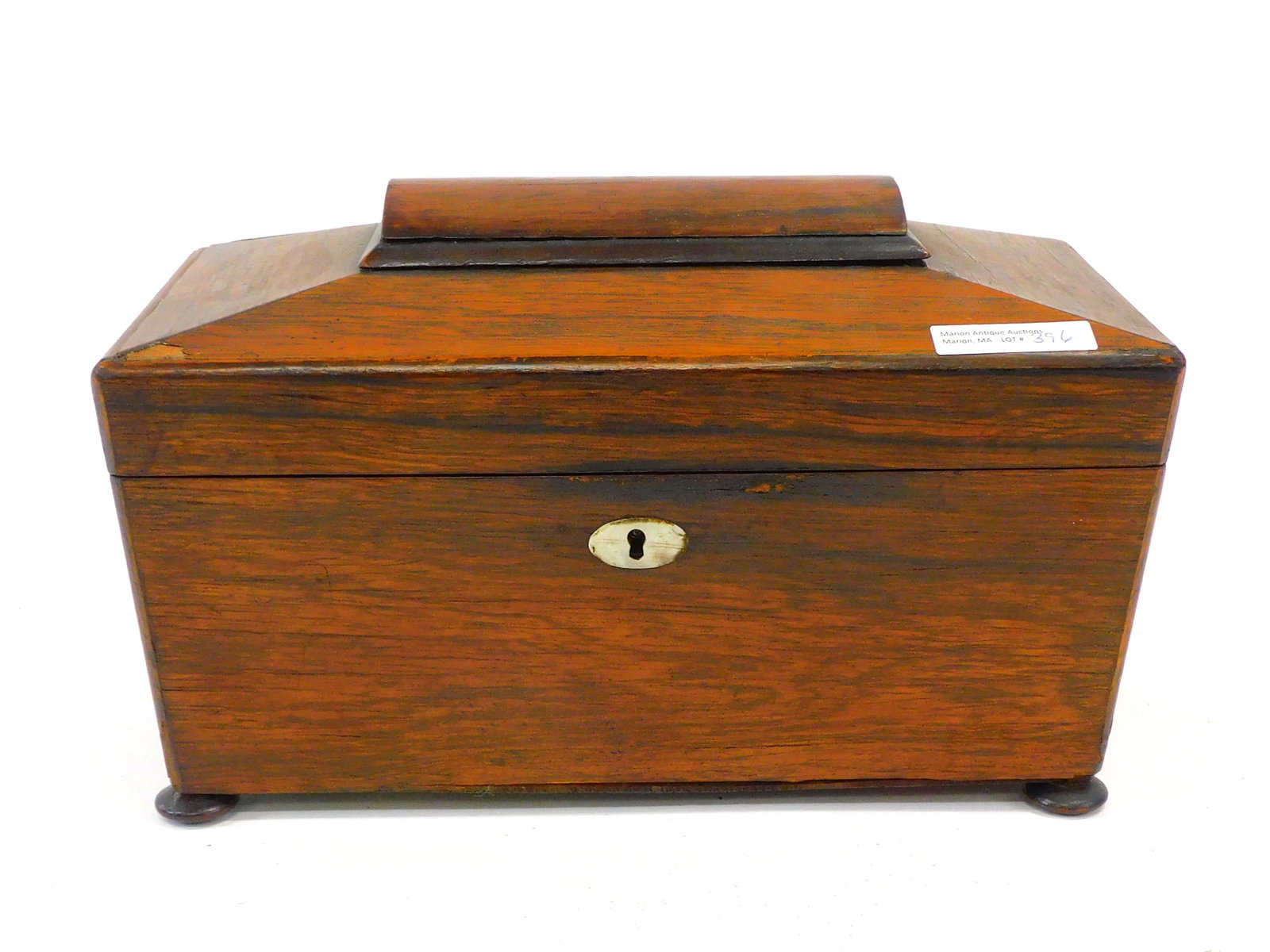 Rosewood Tea Caddy. 19th century. Hip top, canted: sides, and ball feet. Fitted interior with replaced mixing bowl and a sterling spoon. 7" high by 12" wide by 6" deep. Minor loss to veneer. Age appropriate wear.