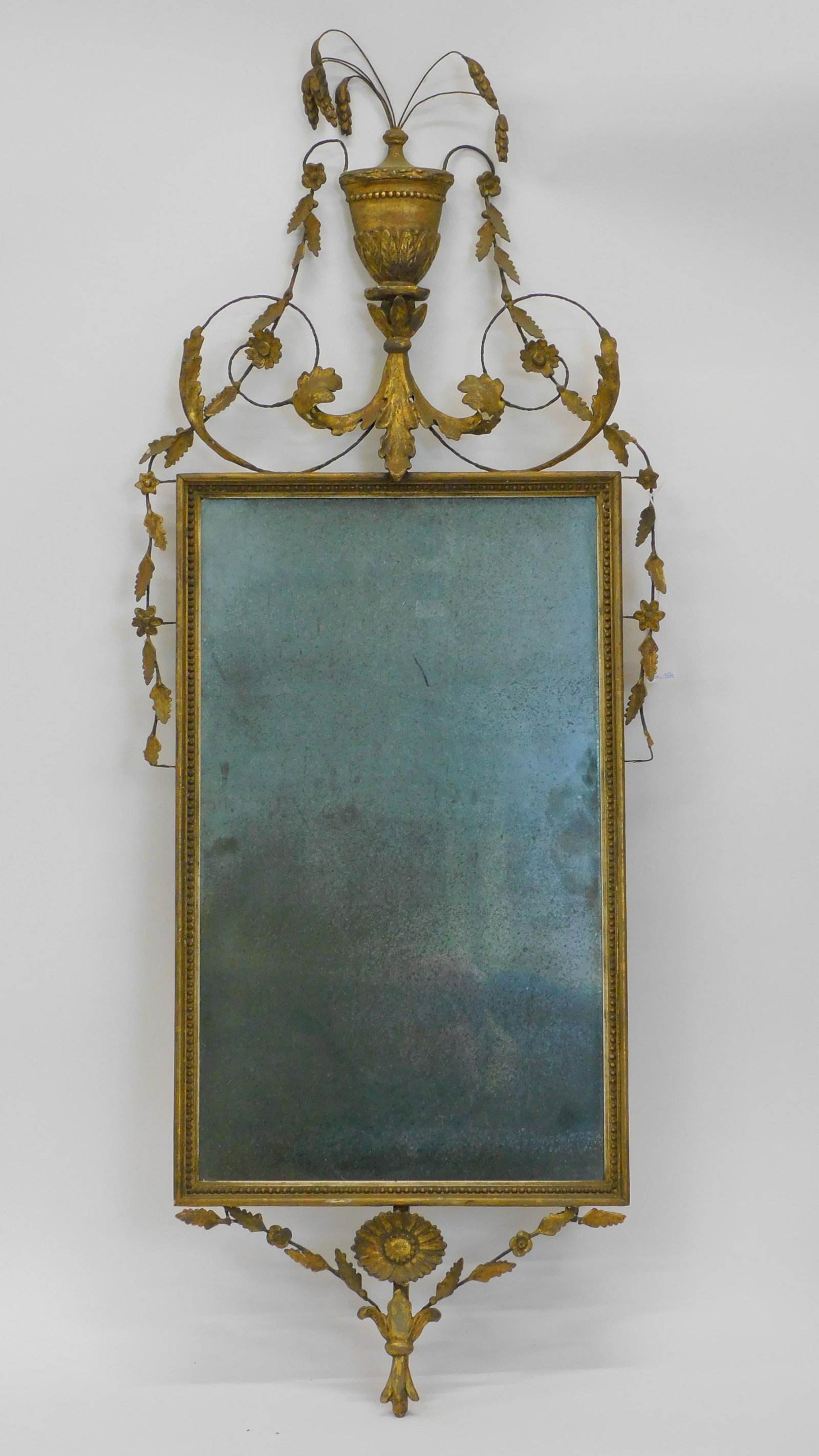 A 19th-century gilt and gesso looking glass. Worn: gold gilt decoration. Shows some loss to gesso. With urn and weeping willow top. Leaf and floral decoration. 50" high by 19" wide.