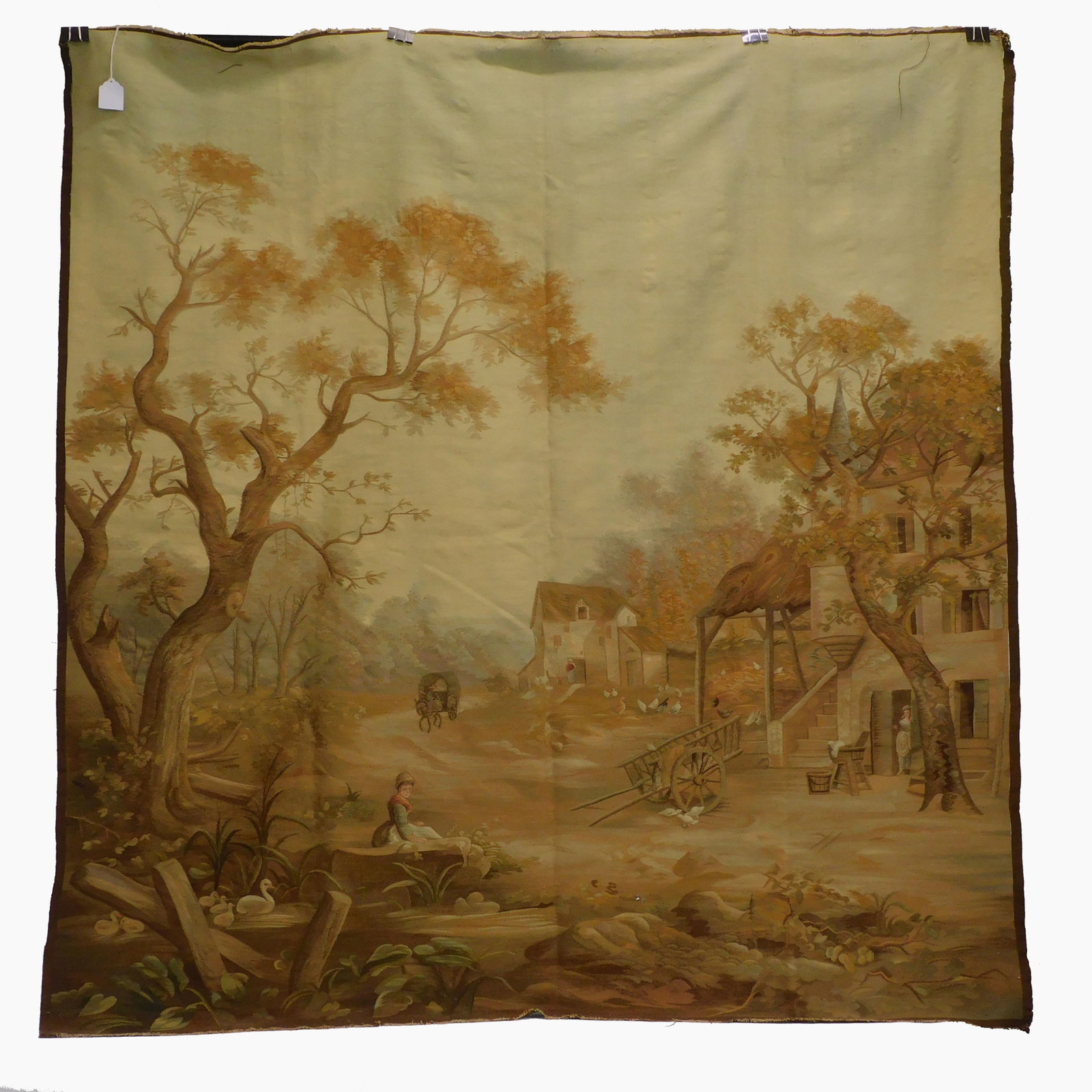 Tapestry in wool. 19th century. Depicting a: romanticized peasant scene. Swans in a stream in the foreground, figures, village homes, and a man on a wagon in the main field and background. Shows some vertical splits. 77 1/2" x 73". Rings affixed