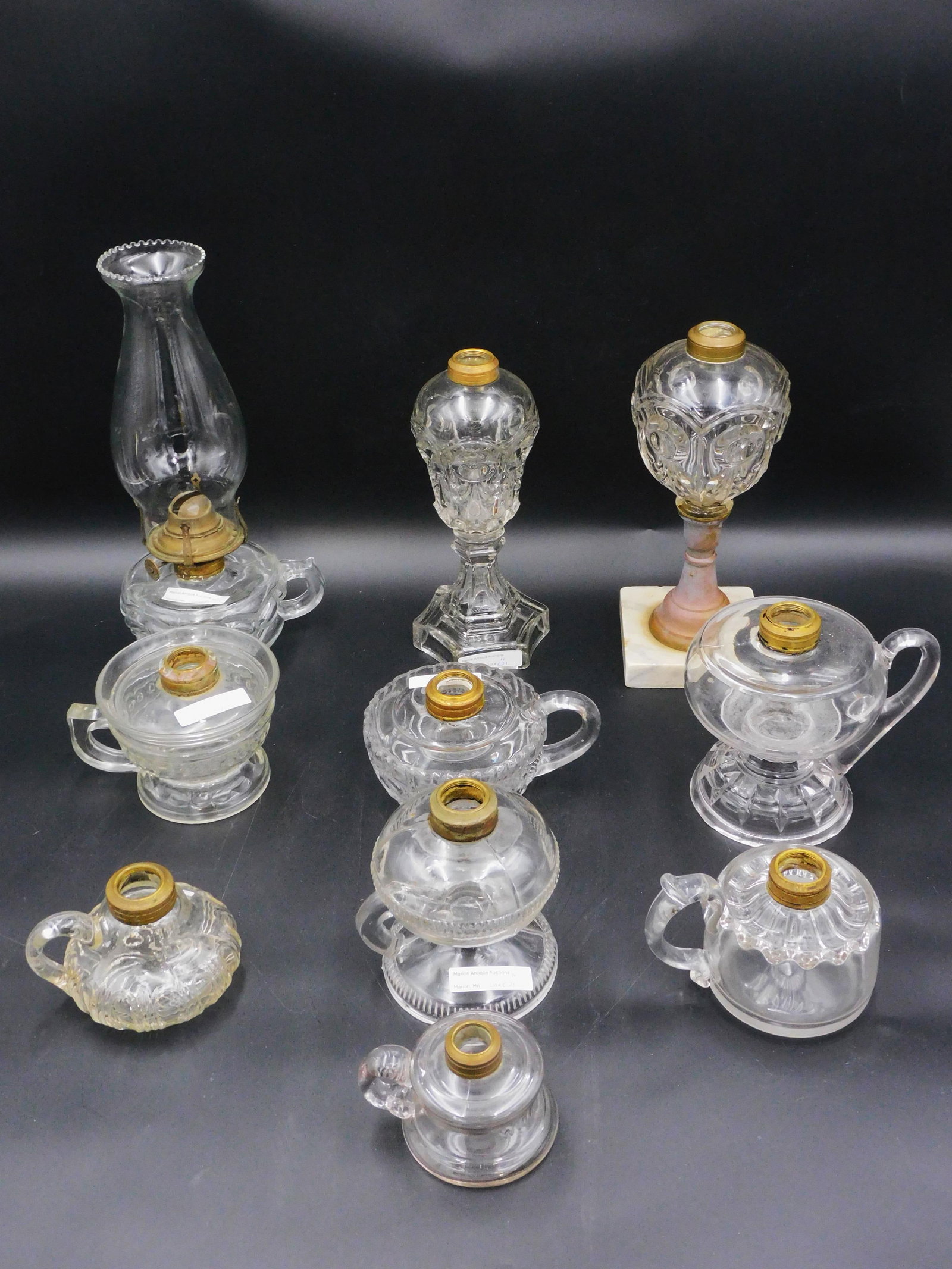 (10) clear glass lamps. 19th century. To include: 8 finger lamps ( 2 3/4" to 5 3/4" high. In patterns such as peanut, "wide awake", etc. Two with applied handles.) Along with an 8 1/2" whale oil lamp, bullseye and plume design. A 9 1/2" bullseye and 