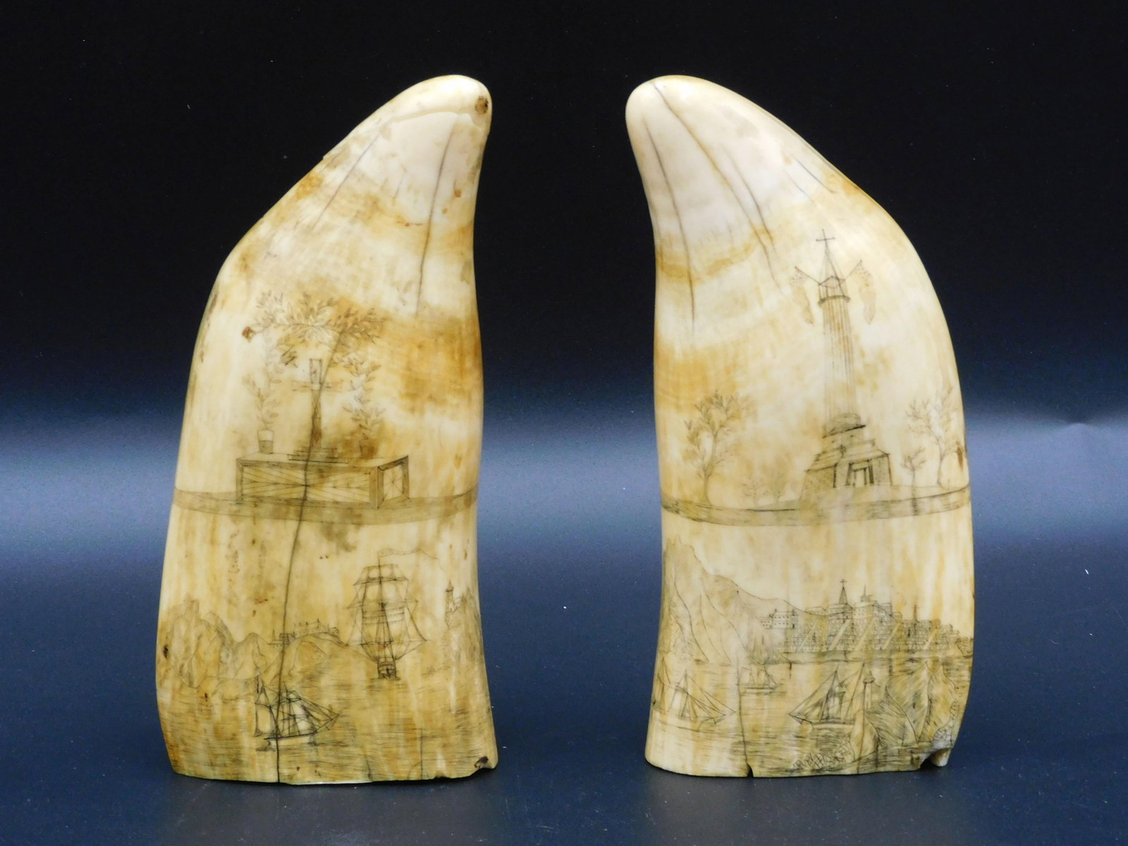 Matched Pair Of Scrimshaw Sperm Whale Teeth: Decorated pair of 19th c. teeth. Decorated with flower filled urn over mountainous harbor scene with paddlewheel steamer in foreground (recto) and memorial tower flying two American flags with continu