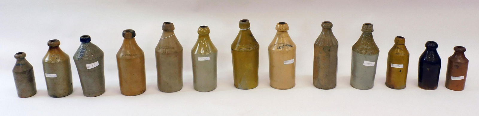 (13) Stoneware Bottles: To include: Dalbecks, A J Gleason 1856 - roughage to top, H Hill and Son, E D Postennes and Co 1872, J Newton and Co California Pop, White Root Beer, Hall and Robbins Hop Beer, Coburn Lang and Co Ging