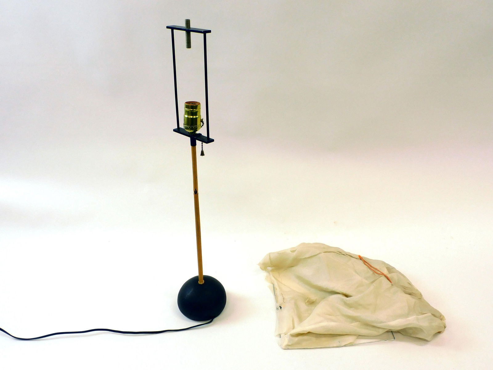 Isamu Noguchi Akari Table Lamp: C. mid-20th c. Cast iron, bamboo. Base is stamped "Made in Japan". Silk shade shows trademark and possible signature of Isamu Noguchi. The shade shows as-is. Deterioration to silk requires conservatio