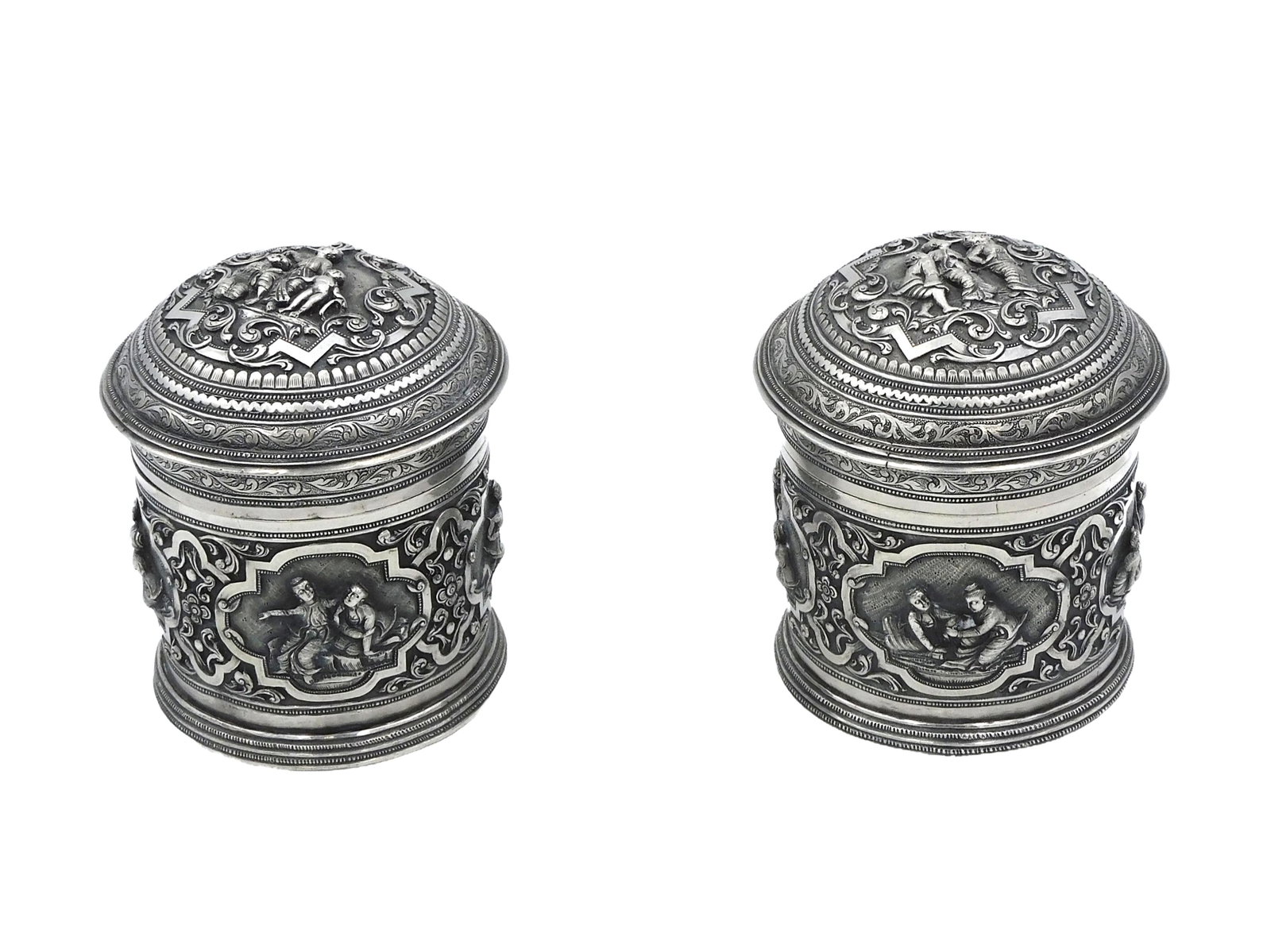 Matched Pair of Asian Silver Betel Boxes: Mid 19th century. Burmese or Indonesian silver covered circular boxes. The boxes and lids are finely engraved, featuring repousse design and vignettes of figures. Finely chased and engraved. Unmarked.