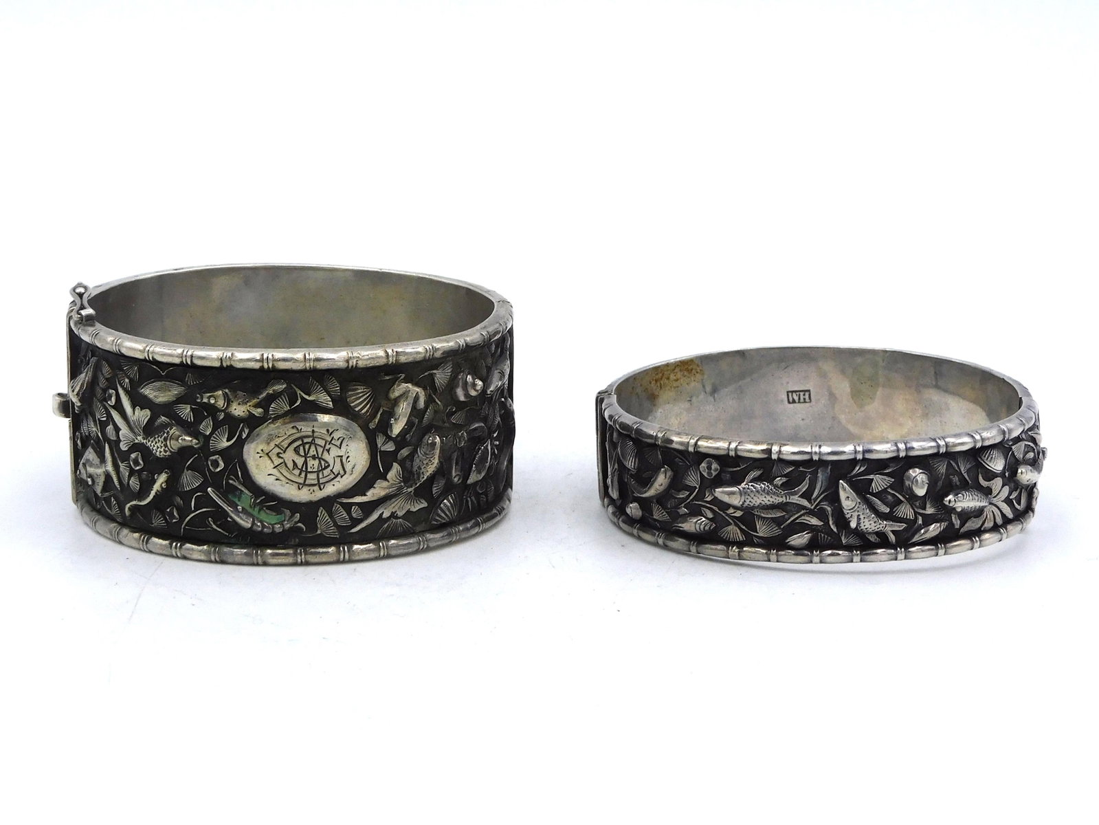(2) Chinese Silver Bracelets: By Wang Hing. Late 19th/ Early 20th century. Post China trade. Two elaborately chased Chinese silver bracelets with fish, mollusks, sea shells, lobsters and crabs. With bamboo borders. The smaller bra