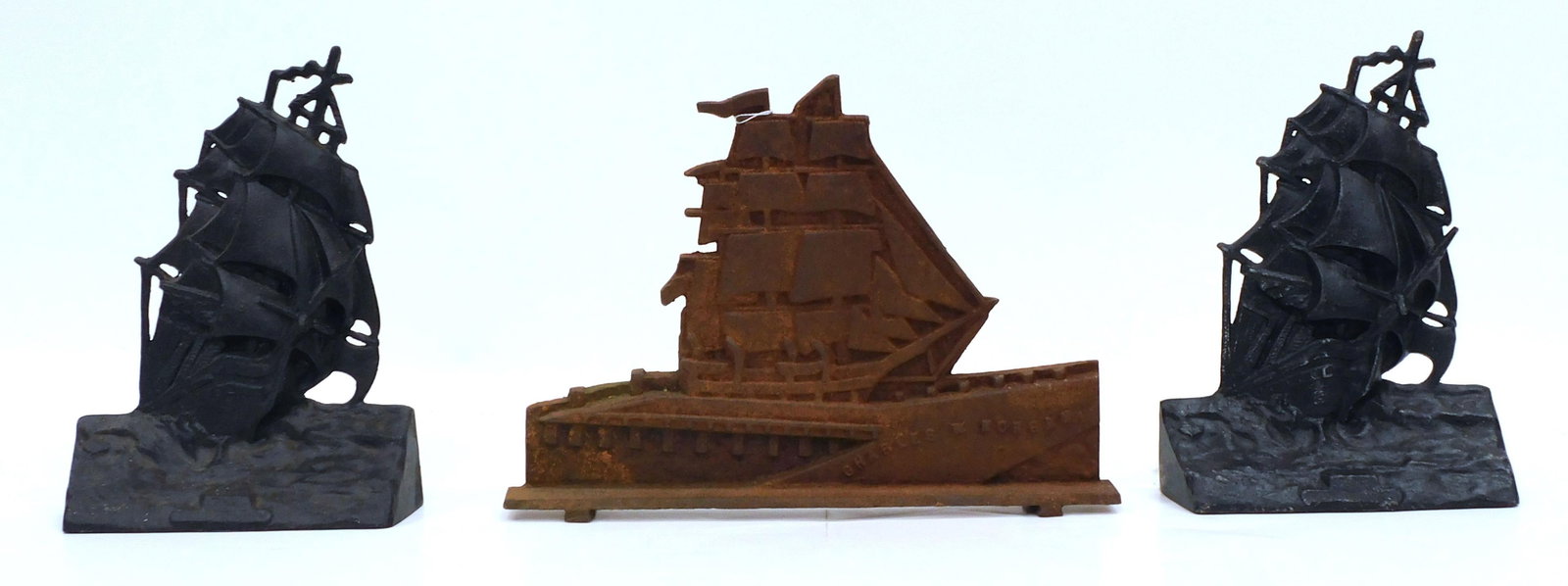 (3) Cast Iron Doorstops: Two are of the USS Constitution. A.M. Marked 1924, Greenblatt Studios, Boston. 11 1/2" high. The other is the Charles W. Morgan. Marked "P.F. Gay, North Dartmouth, MA. Copyright 1932". 11" high x 14 3