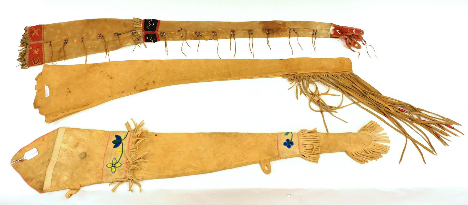 (3) Great Lakes Rifle Sheaths: To include: A) Trade cloth bands with beaded geometric designs. Fringe with bead decoration. 53" long x 7 1/4" wide at top. Shows moth damage and some discoloration. B) Colorful floral beaded decorati