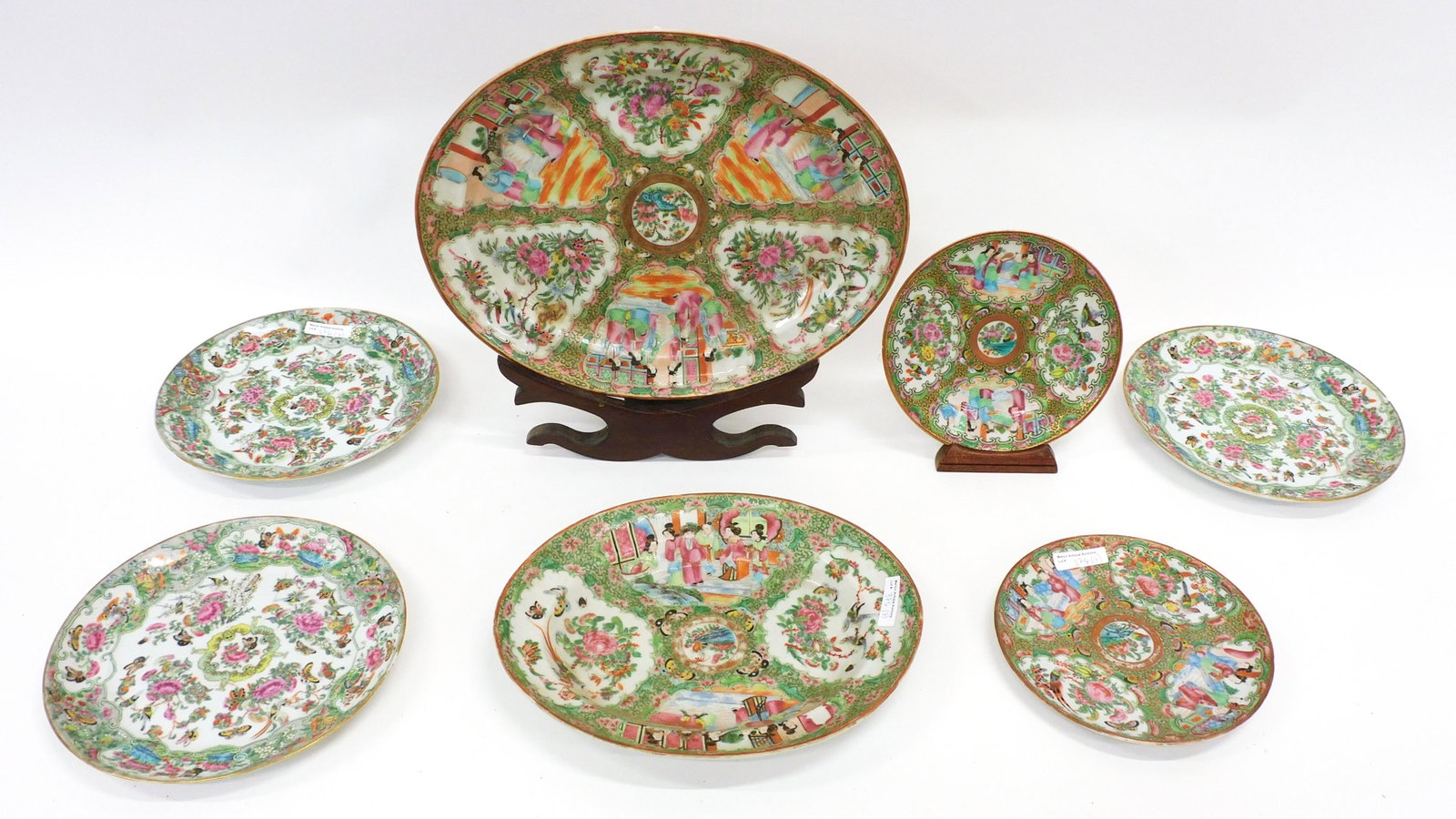 (7) Piece Rose Canton Plates and Platters: To include: (A) Large oval platter. 1 1/2" high x 16" long x 12 1/2" deep. Comes with a wooden plate stand. (B) Oval platter. 1 3/4" high x 12 1/2" wide x 10" deep. (C) Dinner plate. 10" diameter. (D)