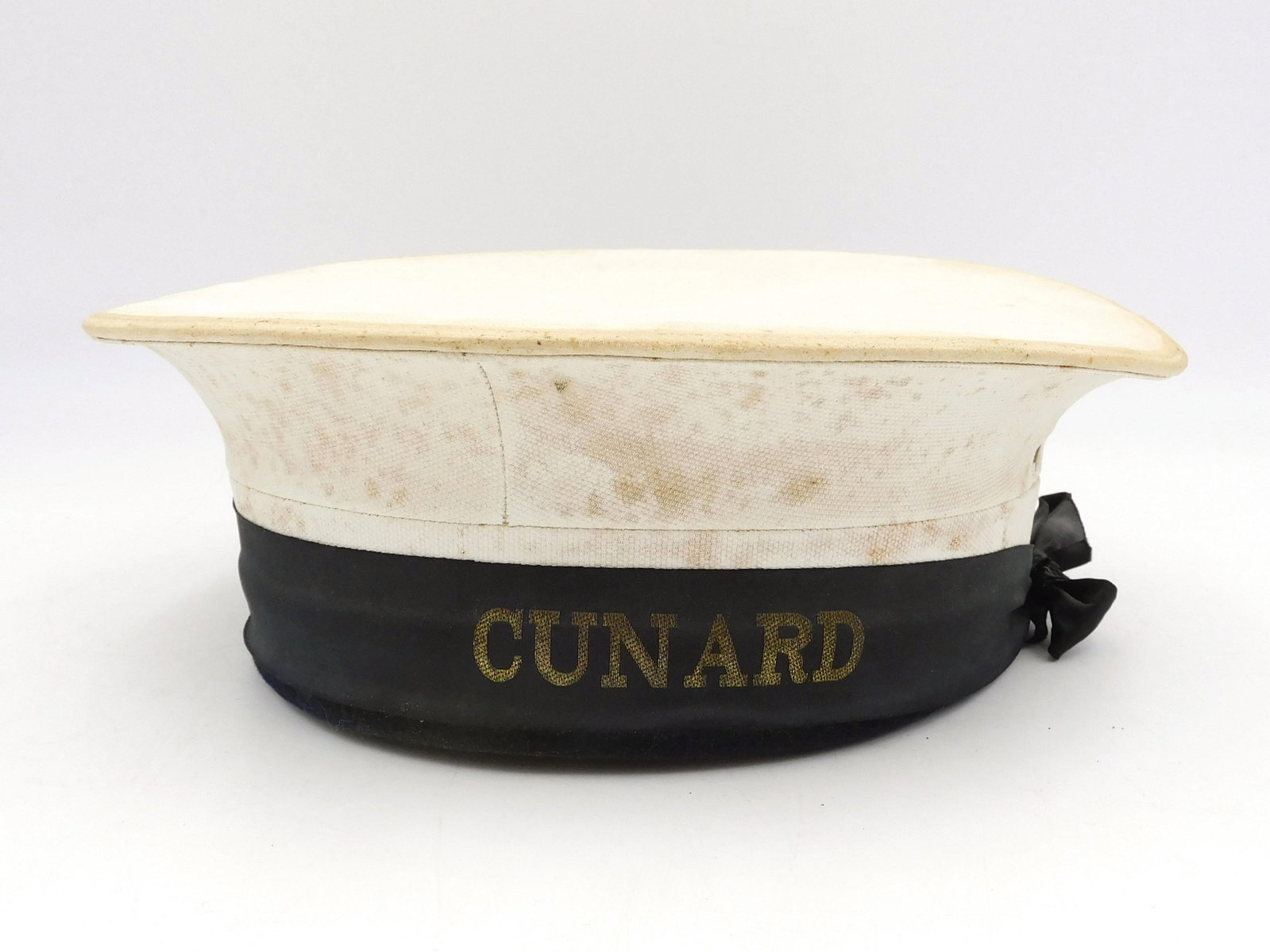 Cunard Crewman's Hat: 20th C. Cunard steamship line hat. White with black trim and gold lettering, 3 1/4" high x 10" diameter.