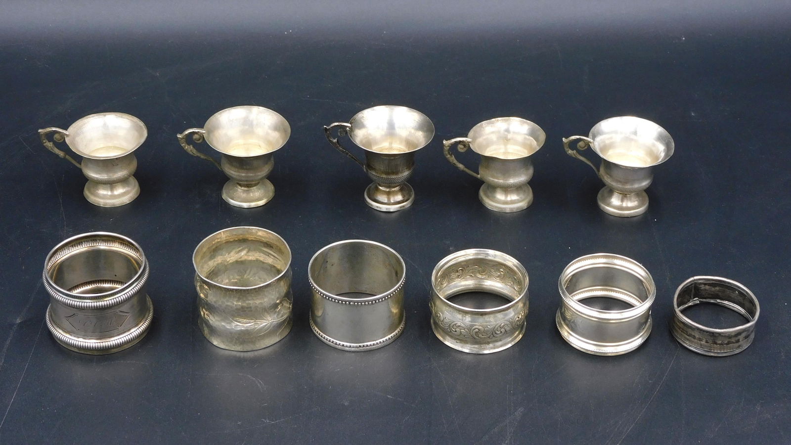 (11) Piece Silver Lot: To include: (A) Two 19th C. napkin rings marked sterling. One is hand hammered with floral design. (B) Four 19th C. napkin rings. Tested silver. (C) Five sterling cups with handles. 5 1/2" high. Total