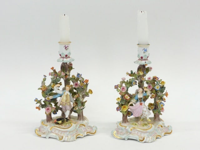 Pair of Meissen Candlesticks: 19th C. One depicts a male gentleman; the other his female companion. Ornate floral and tree trunk design. The backs have finger handles made as part of the tree trunk.