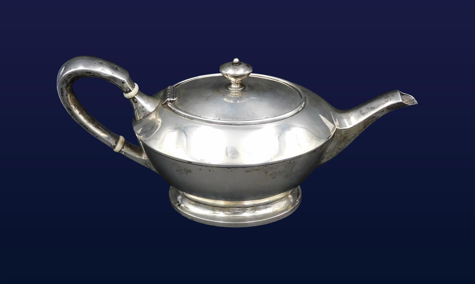Sterling Silver Teapot: Early 20th C. Stamped on bottom Bailey Banks & Biddle Co., Philadelphia. Low profile form, featuring a domed disc finial, scroll handle, tapered spout and raised foot. 5" high x 11" wide. 16.0 ozt.