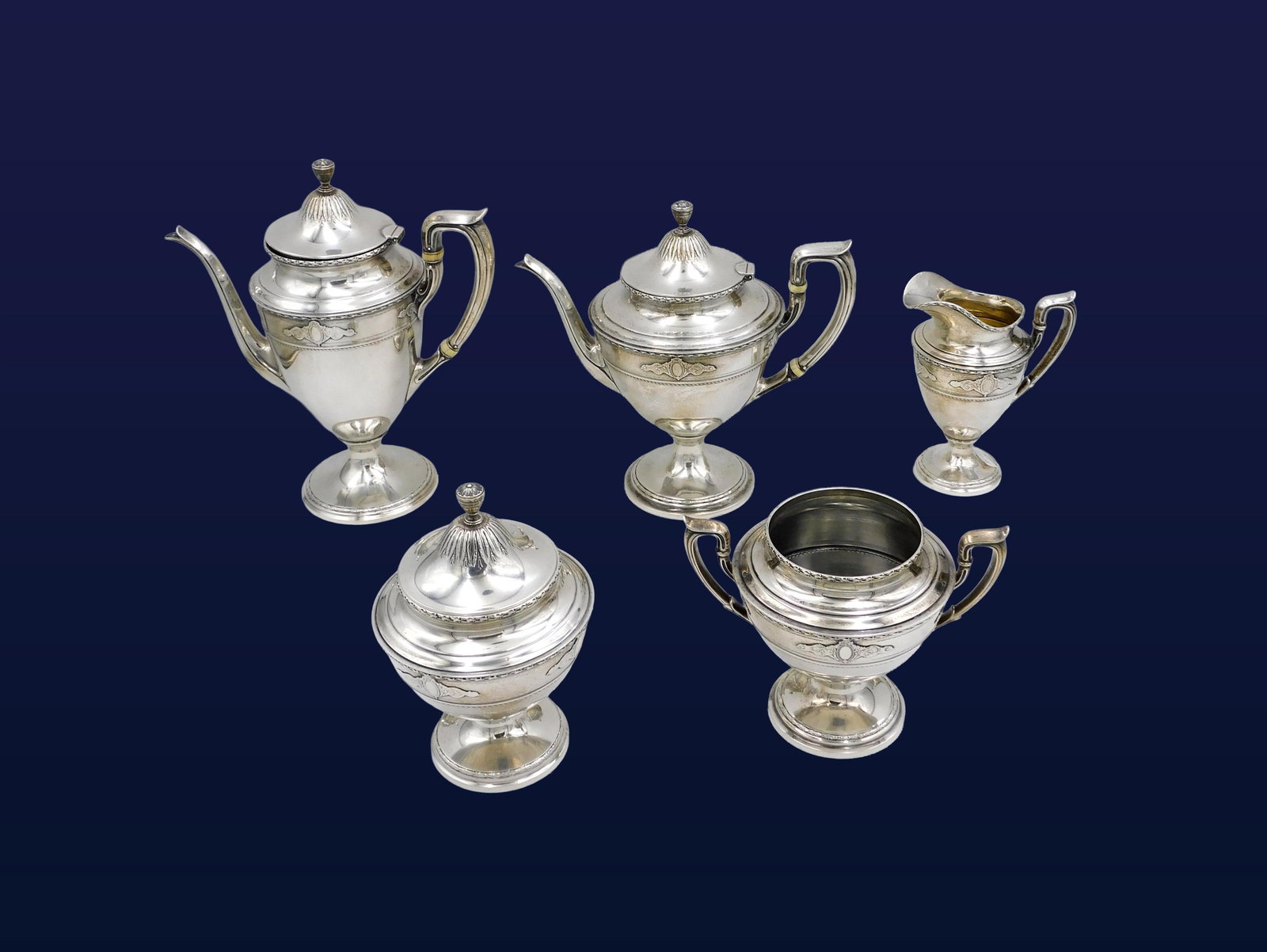 (5) Piece Reed & Barton Sterling Tea Set: Late 19th/Early 20th C. Sterling silver. Reed & Barton hallmark. The bodies are ornamented with applied rococo cartouches, bright-cut engraved banding, and textured fields. The domed covers are decora