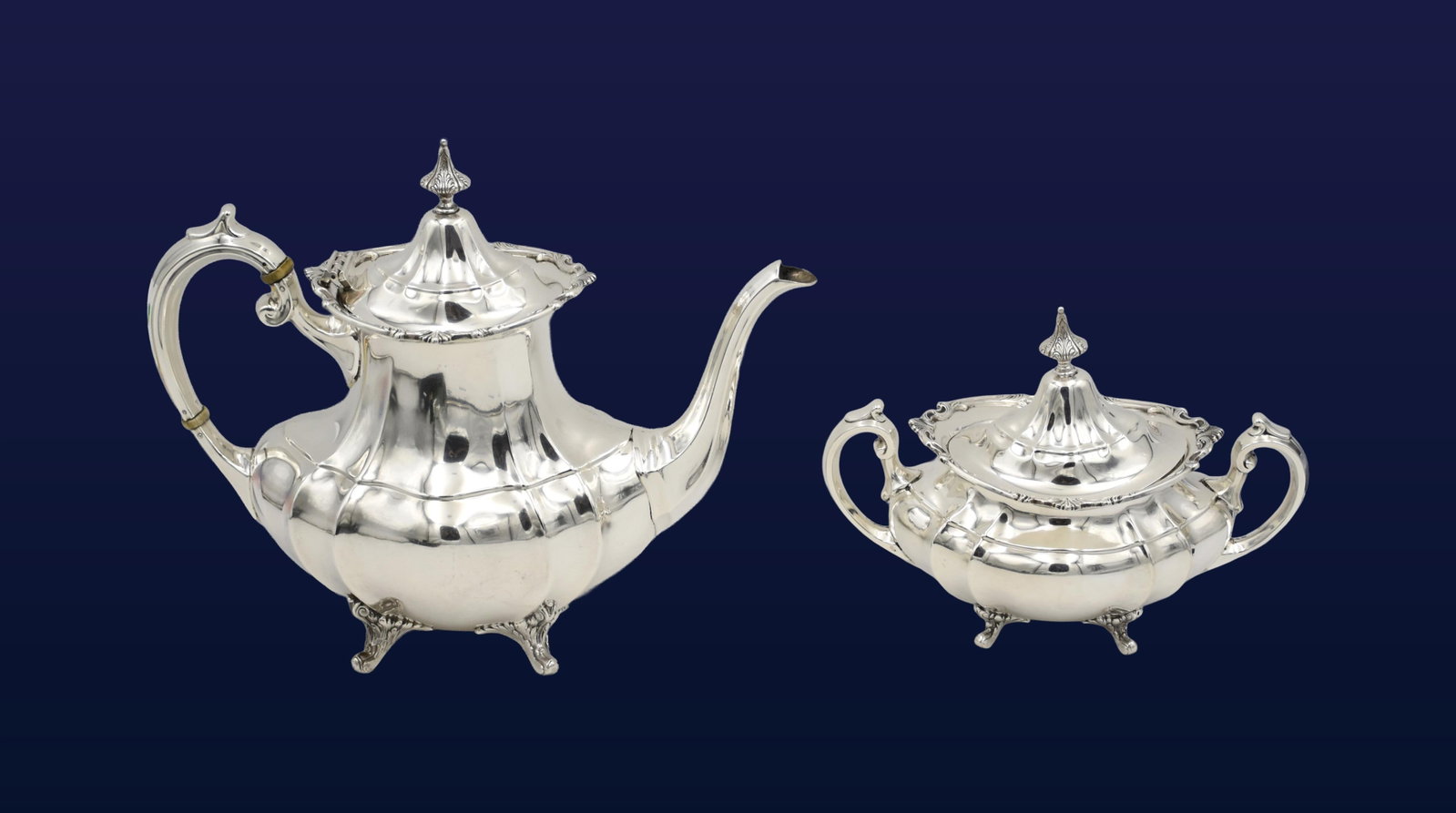 (2) Piece Reed & Barton Sterling Tea Service: 20th C. Hampton Court pattern. Each with ornate scroll handles, paw feet, and domed covers with decorative finials. To include: (A) Teapot with hinged lid. 9" high x 10 1/2" wide handle to handle. (B)