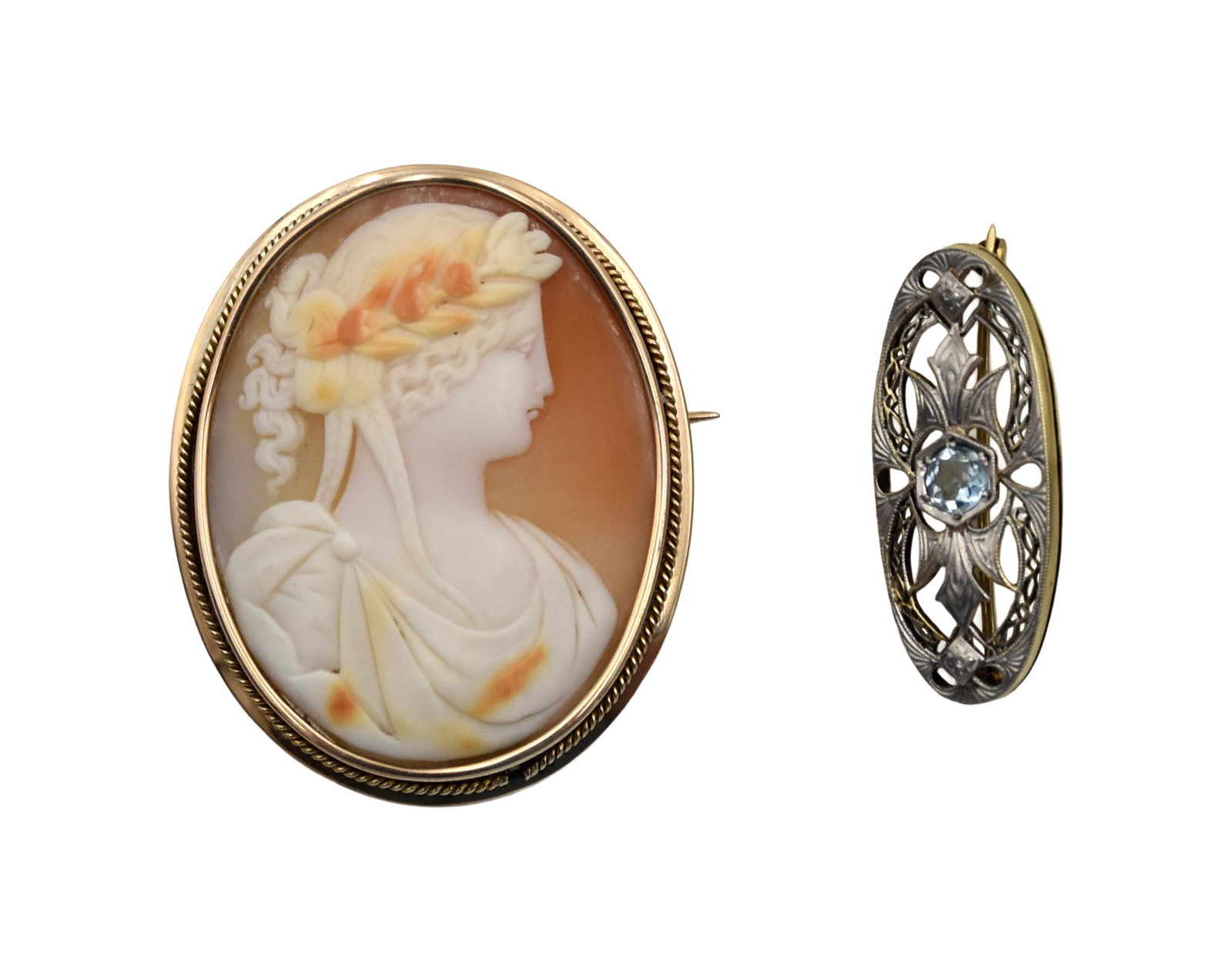 (2) Antique Brooches: 14kt gold. To include: (A) Shell cameo brooch depicting a Greco-Roman woman with laurels set in a gold frame. 2" long x 1 3/4" wide. 12.26 total grams. (B) Art Noveau brooch pin. Yellow and white