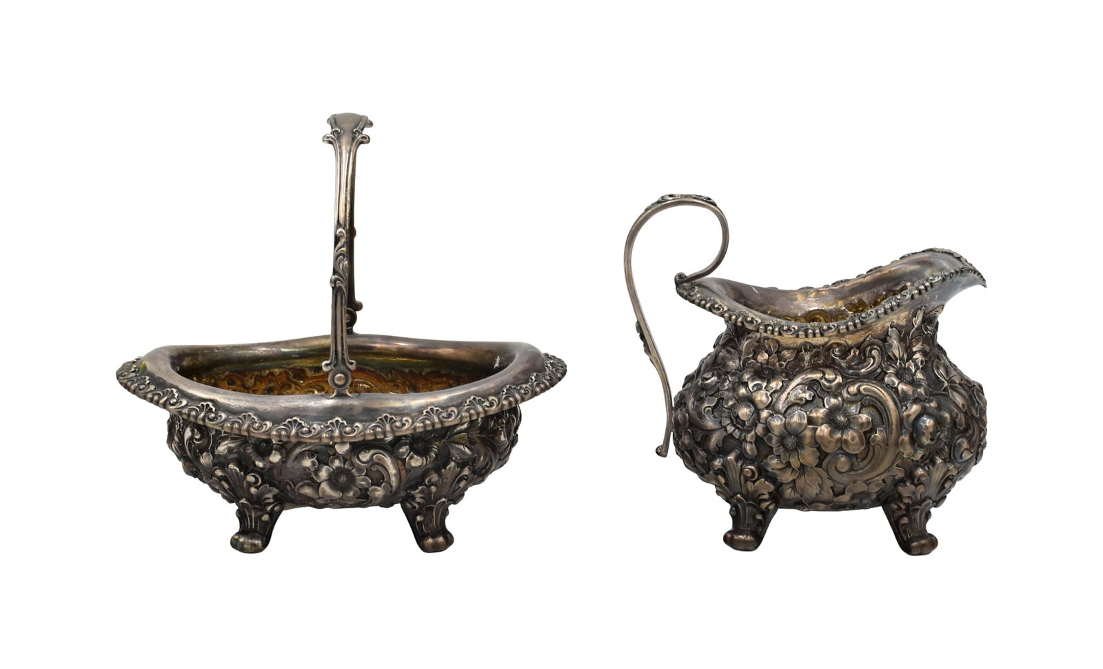 (2) Repousse Sterling Silver Pieces: 20th C. To include: (A) Footed creamer. 5" high x 5 1/4" wide x 3 1/2" deep. (B) Footed winging basket. 5 3/4" high with handle up x 6 1/2" wide x 4 3/4" deep. 18.84 total ozt.Age appropriate wear.