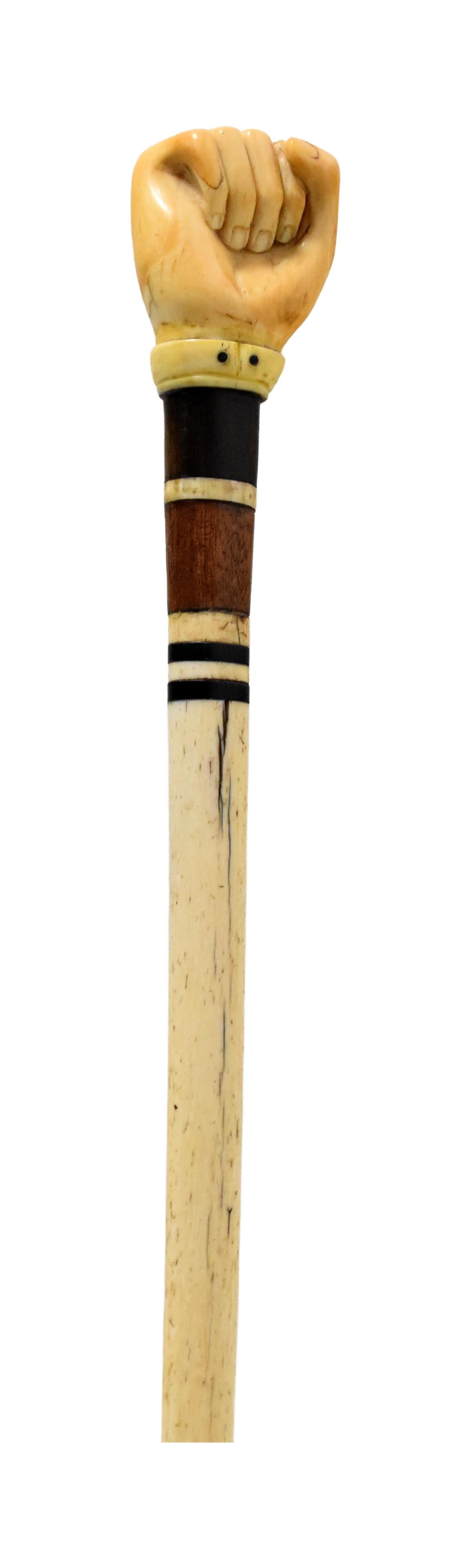 Sailor-Made Walking Stick: 19th C. Clenched fist handle from a whale's tooth. Exotic wood band. Baleen bands. Bone shaft. 35 1/2" long x 2" wide at fist. Good condition. Possible restoration to shaft. Shipping restriction: