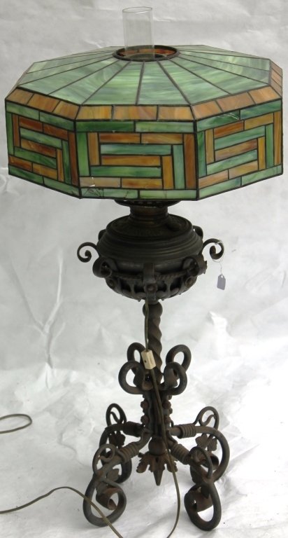 AMERICAN LATE 19TH C BANQUET LAMP, WROUGHT IRON: BASE; BRASS FONT; LATER LEADED GLASS SHADE WITH MULTIPLE DAMAGES TO THE GLASS; 32 1/2" HIGH, 18" SHADE