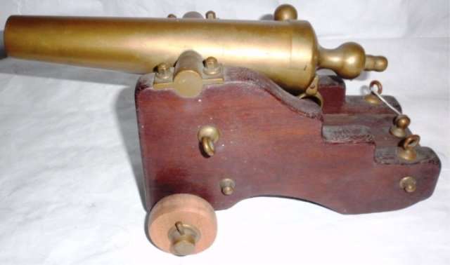 BRONZE SIGNAL CANNON WITH WOODEN CARRIAGE,: MARKED NEW HAVEN, CT, PAT. 1890. MAKER'S NAME IS WORN AWAY. OVERALL MEASUREMENTS: 15" LONG, 8 1/2" WIDE. GOOD CONDITION WITH ONE REPLACED WOODEN WHEEL AND ONE BRASS EYE HOOK MISSING.
