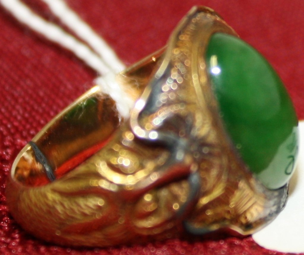 14K YELLOW GOLD CHINESE MAN'S RING WITH OVAL: GREEN JADE STONE, INTERESTING TEXTURED MOUNT WITH FACES ON SIDES OF THE STONE. SIZE 11, 9.3 DWT. RING HAS BEEN CUT AND SIZED.
