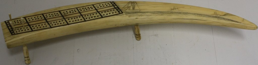 19TH C CARVED WALRUS TUSK CRIBBAGE BOARD: DEPICTING RELIEF CARVED SHIPS AND LIGHTHOUSE. 17" LONG. FROM THE IPPOLITO COLLECTION.
