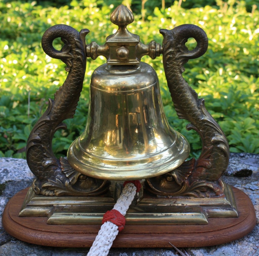 20TH C BRONZE BELL WITH DOLPHIN SUPPORTS, WOODEN: BASE. SAILOR MADE ROPE PULL. 14" HIGH, 16" WIDE, 7 1/2" DEEP.