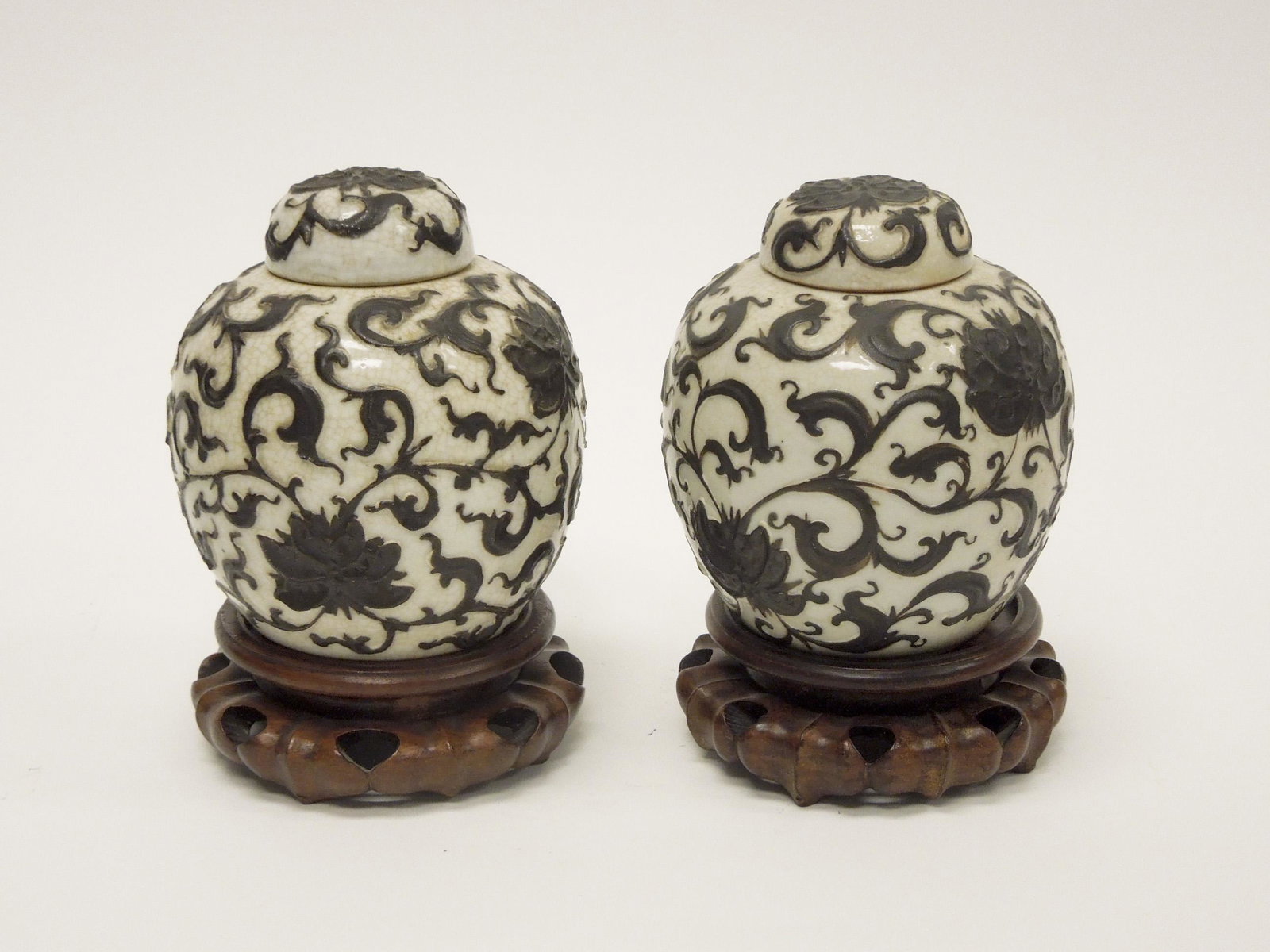 Pair of Chinese Crackle Glaze Jars.: Pair of Chinese porcelain crackle glaze lidded jars with floral overlay decoration. On wood stands. 6" tall.