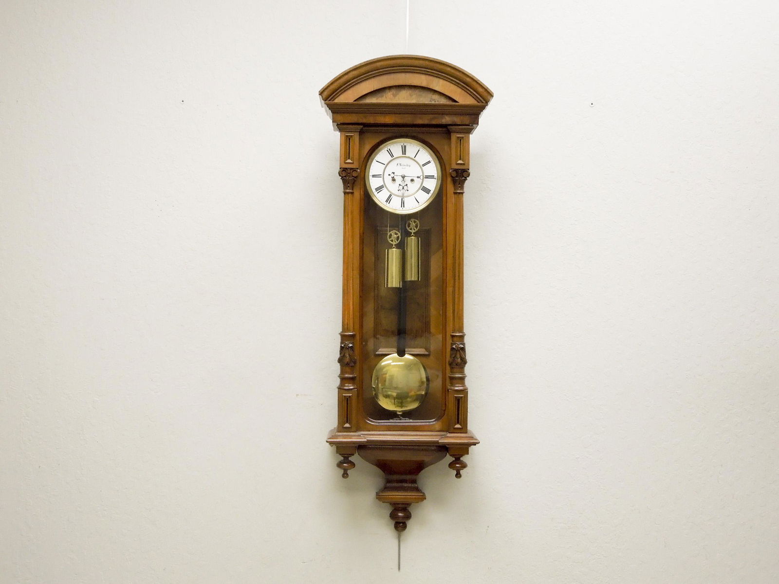 Late 19th / Early 20th C. Vienna Wall Clock.: Late 19th / Early 20th C. Vienna Wall Clock. F. Brischig Wien. Walnut case with an arched crest. Circular face with time and strike. Two weighted pendulum movement. 48" x 15".