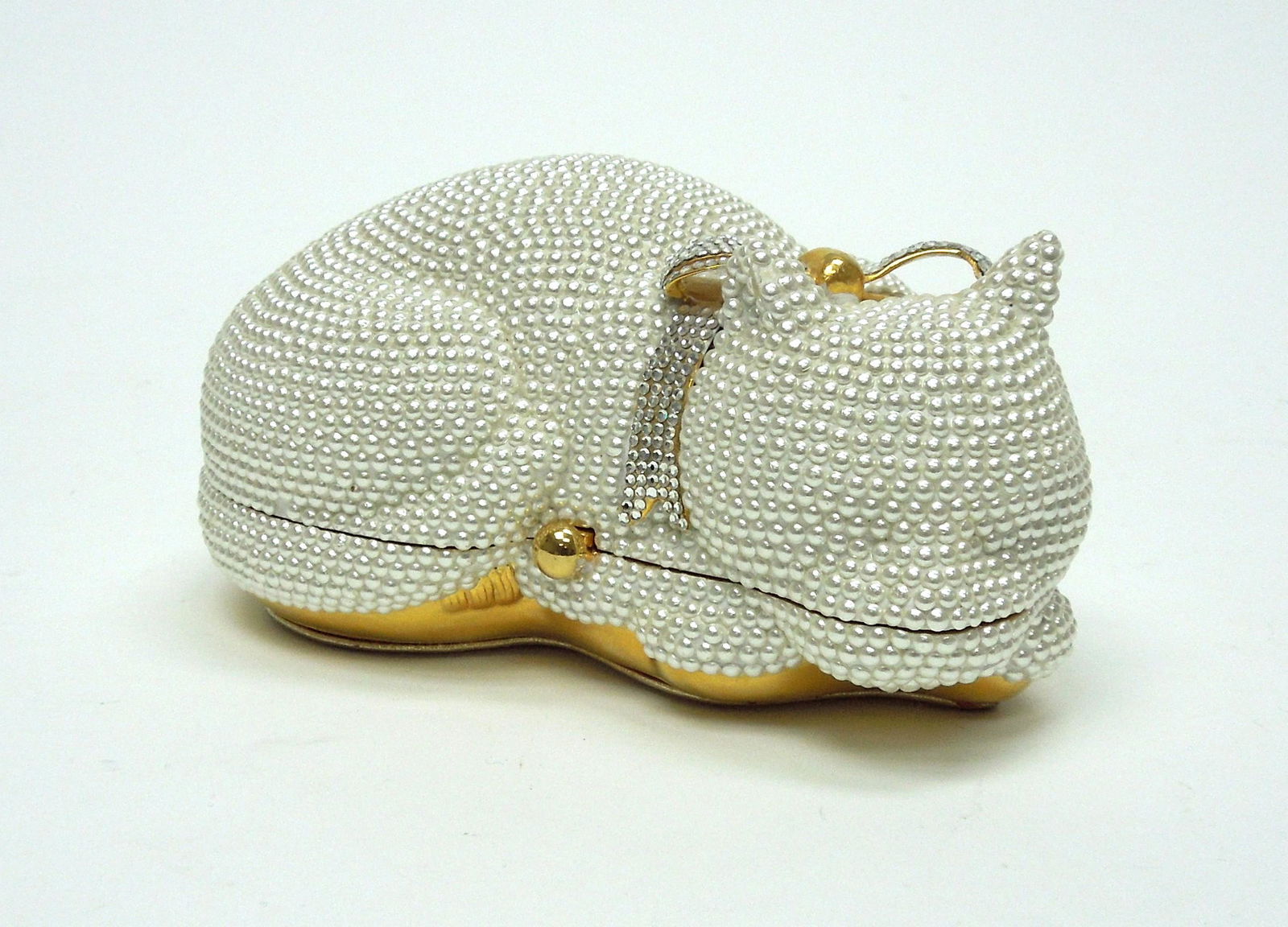 Judith Leiber Minaudiere Cat Clutch.: Judith Leiber sleeping cat form clutch. White faux pearl encrusted exterior with rhinestone bow-knot collar. Gold leather lined interior with comb and coin purse.