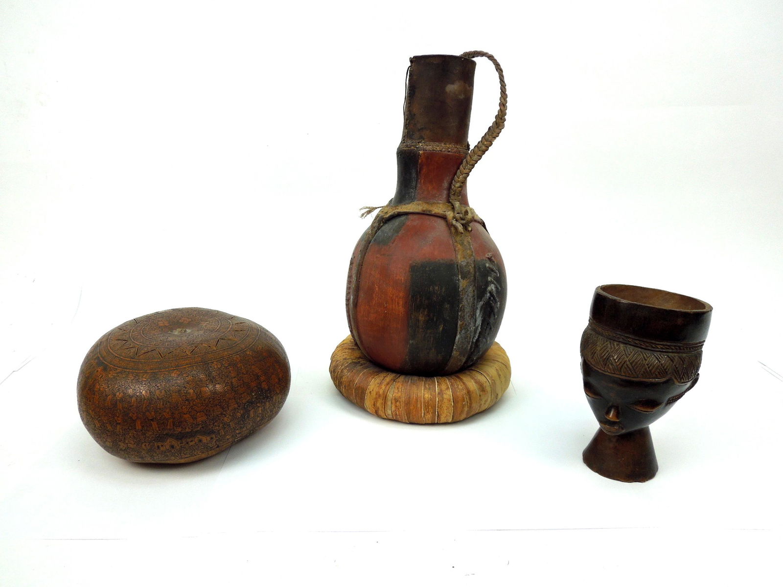 Group of African Oceanic Items.: Group of African items, including a finely carved wood figural mug; an intricately tooled dried gourd box; polychrome carved gourd vessel with braided hide strap work.