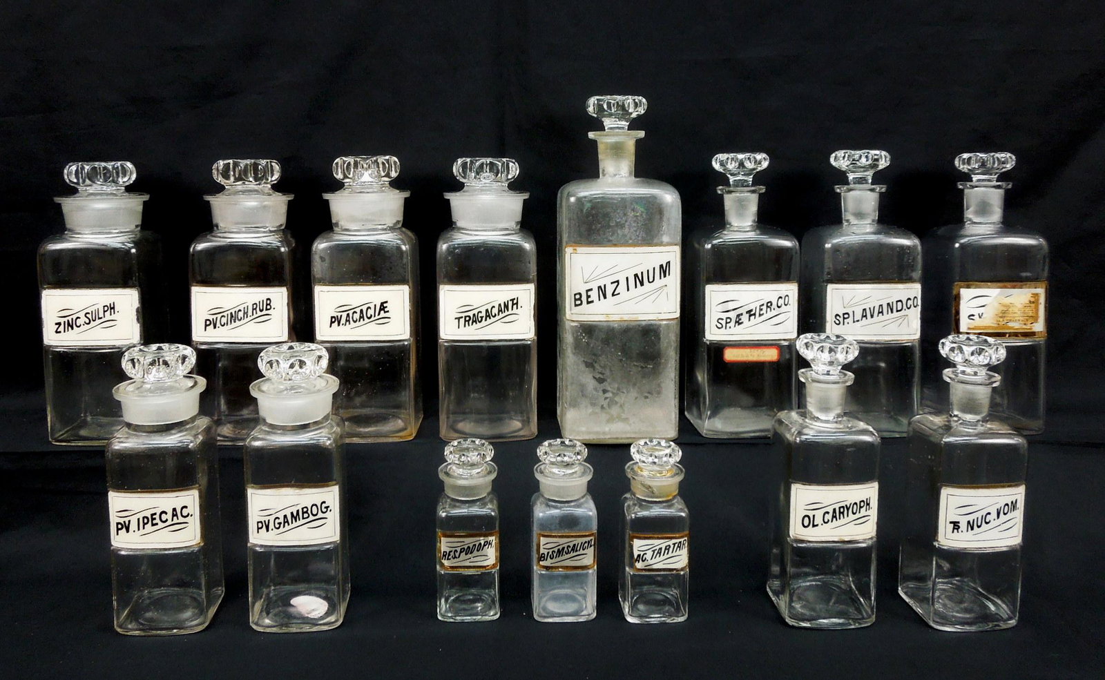 (16) Antique Apothecary Store Jars.: Group of (16) antique apothecary store jars with stoppers, most with labels under glass. Various sizes. Tallest: 12 1/2".