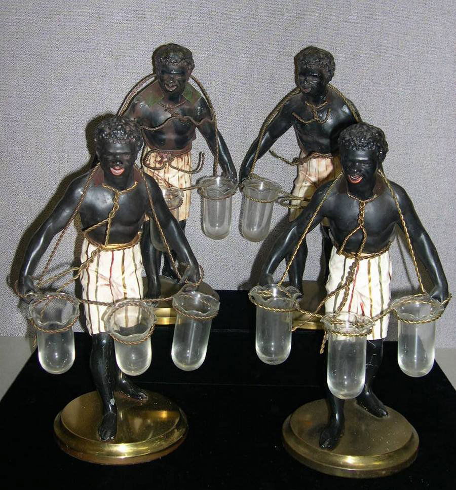 Blackamoor Epergnes: Group of 4 patinated and polychrome metal figural epergnes modeled as Blackamoors with metal rope yokes, each inset with 3 glass trumpet form vessels, on metal plinths. Maker’s mark on backside of f