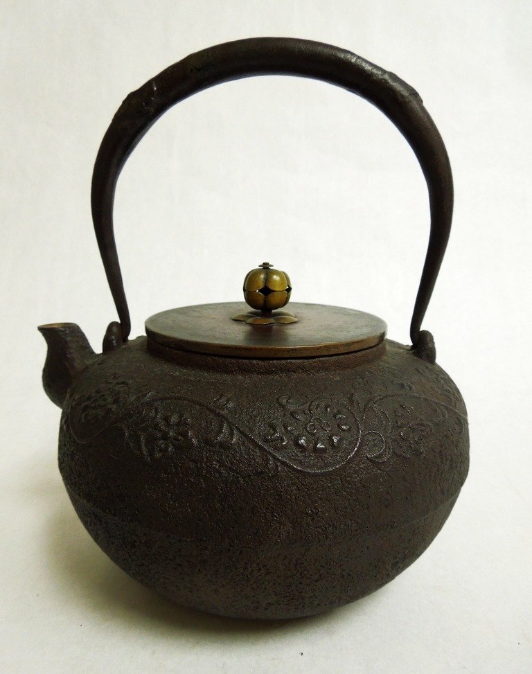 Japanese Iron Tet su ban: Japanese cast iron tetsuban (tea pot) with raised decoration and swing handle. Bronze and copper lid, with cipher signature on the underside of lid.