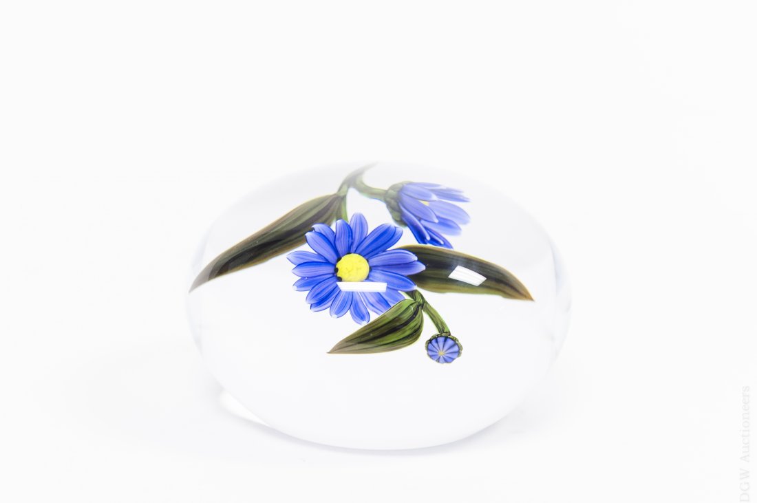 Buzzini Art Glass Paperweight.: Chris Buzzini art glass paperweight. Depicts two purple flowers and one bud. Etched: Buzzini ’99 TD B/25 (Approx. 2" x 3 1/2"). From the Collection of Eric Sinizer.