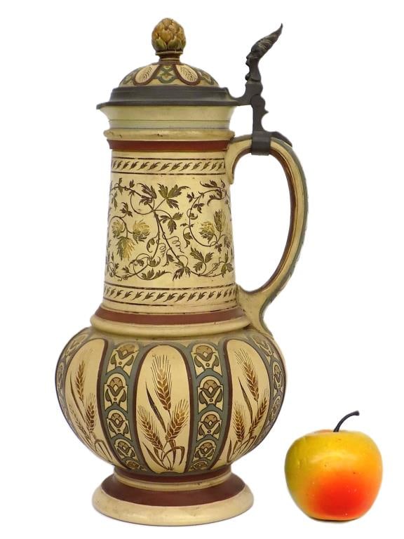 BIG METTLACH BARLEY & HOPS BEER STEIN No 1977: Big Mettlach Stein No. 1977 Entitled Barley and Hops. Relief and Incised Pottery Signed M. Hein. Inlaid Lid with Barley Finial. Pewter Mask Form Thumb Piece. Base Marks. Height 14.25"