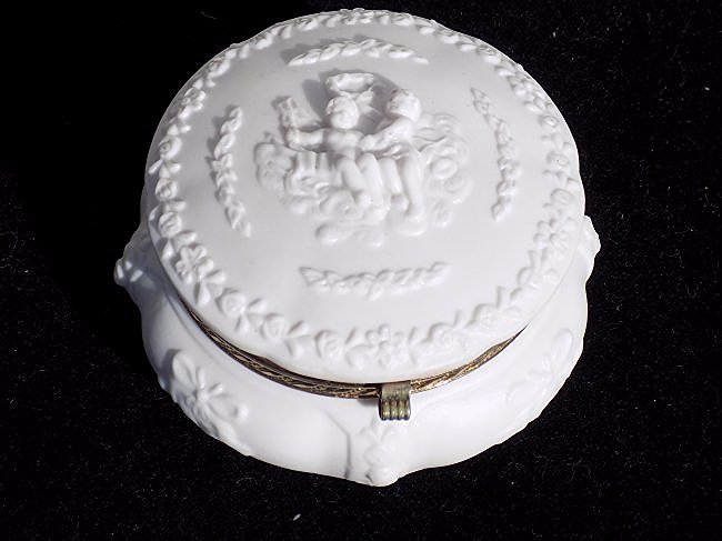 ANTIQUE BISQUE PUTTI LIDDED DRESSER BOX: Antique porcelain bisque lidded dresser box . Decorated with puttis, ribbons & garland with gilt metal ormolu. Base numbered. H 2 1/2" x D 4"