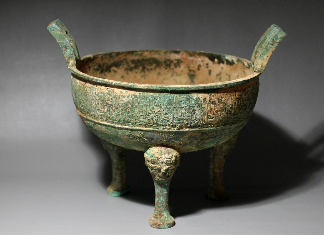 BRONZE DING: Tripod base and loop handles. Body decorated by raised flanges. Height: 12.25"