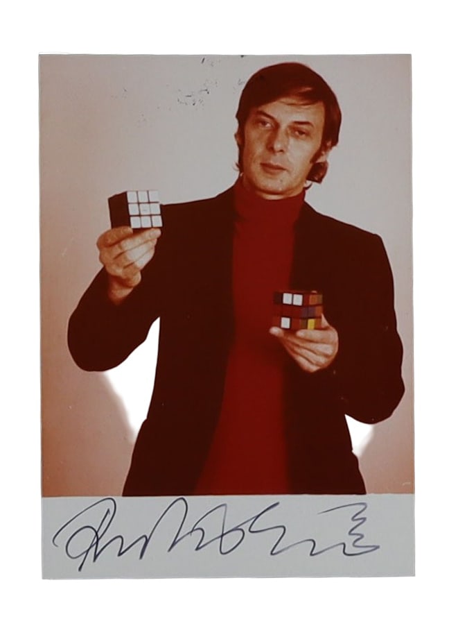Ernő Rubik Signed Photograph Holding Two of His Famous Cubes: Ernő Rubik Signed Holding Two of His Famous Cubes. Ernő Rubik (b. 1944), Hungarian inventor, architect, and professor who created the Rubik's Cube in 1974. Signed in black ink on the lower w