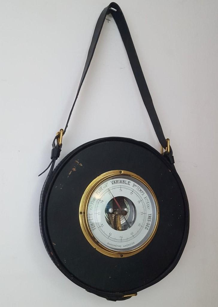 Jacques ADNET - vers 1955 Baromètre en laiton,: Jacques ADNET - vers 1955 Baromètre en laiton, verre et cuir noir piqué sellier blanc, de forme circulaire à lanière formant attache retenue par trois boucles stylisées. 50 x