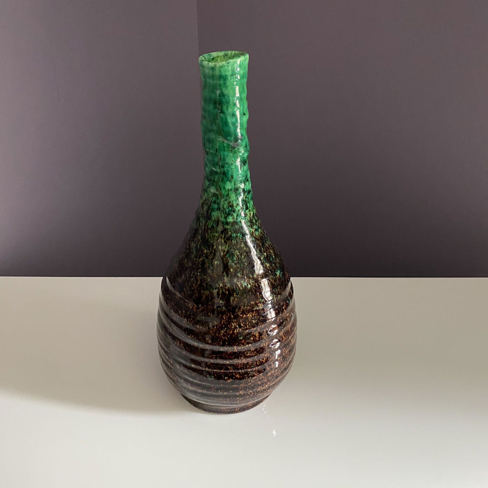 ACCOLAY Vase à long col en faïence à: ACCOLAY Vase à long col en faïence à décor moucheté brun et vert en dégradé H : 36 cm *Vendu sur désignation