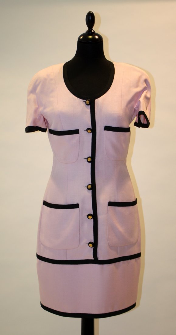 CHANEL Robe en tissu rose, bordures biais noires.: CHANEL Robe en tissu rose, bordures biais noires. Doublée soie rose. Quatre poches plaquées devant. Boutons noirs et or siglées. Taille 38 Très bon état