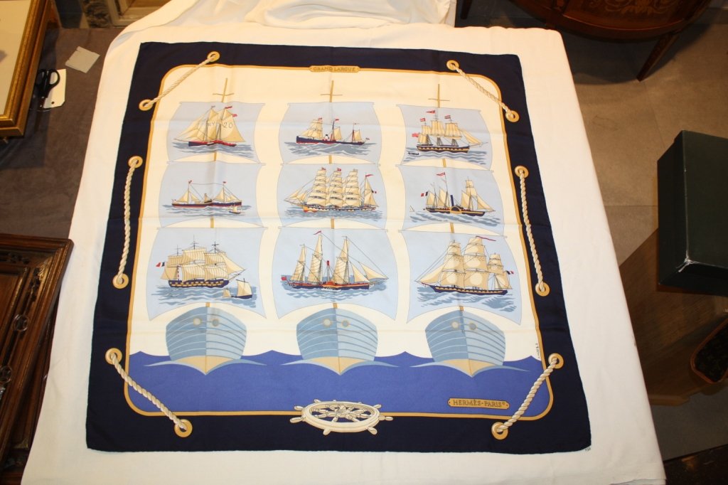 HERMES- Carré en soie imprimée et titré Grand Larg: HERMES- Carré en soie imprimée et titré Grand Largue représentant des voiliers, bordure bleu marine. Très bon état.