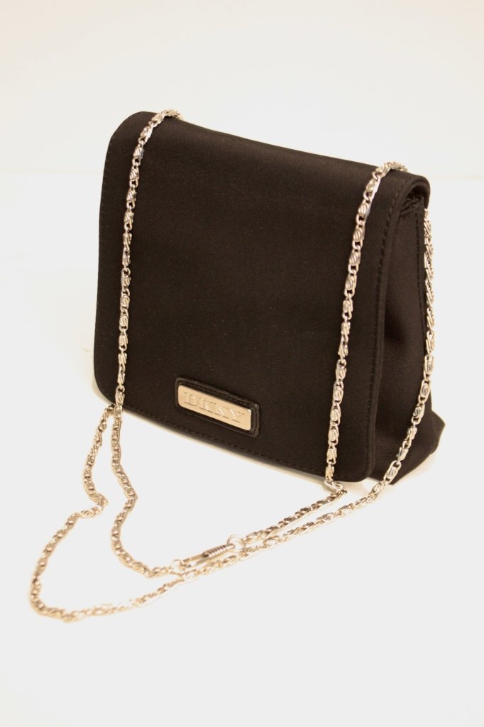 DKNY - Sac à rabat en tissu noir, sigle métal sur le de: DKNY - Sac à rabat en tissu noir, sigle métal sur le devant, fine bandoulière en métal torsadé. Bon état. 15 * 13 cm.