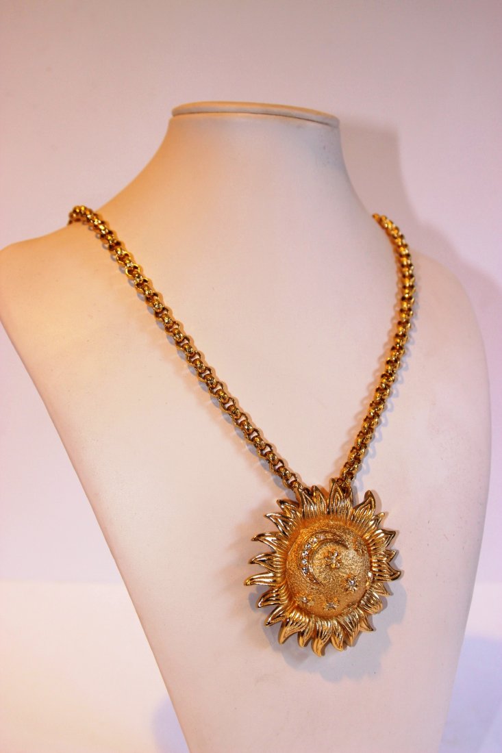 CHRISTIAN DIOR Collier en métal doré composé d'une: CHRISTIAN DIOR Collier en métal doré composé d'une chaine torsadée siglée sur fermoir et d'un pendentif figurant un soleil souriant (pouvant être porté en broche). Bon état