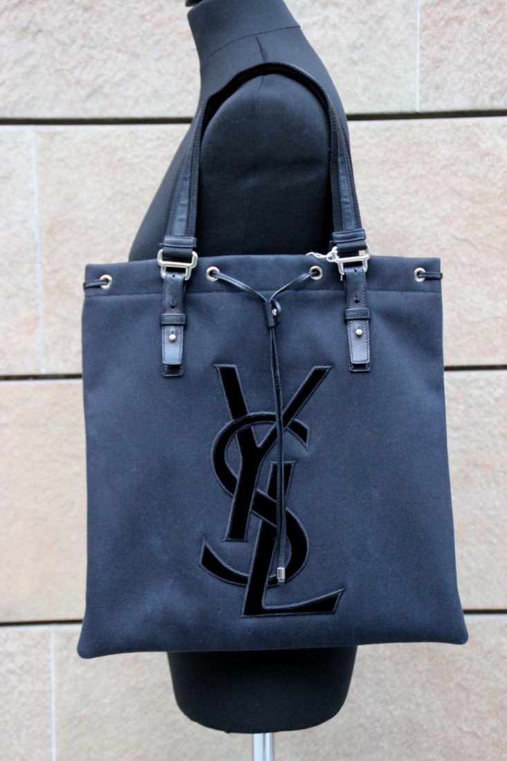 YVES SAINT LAURENT: YVES SAINT LAURENT Sac cabas en toile et cuir noir, un grand sigle YSL sur le devant, deux anses réglables en cuir noir Dimensio