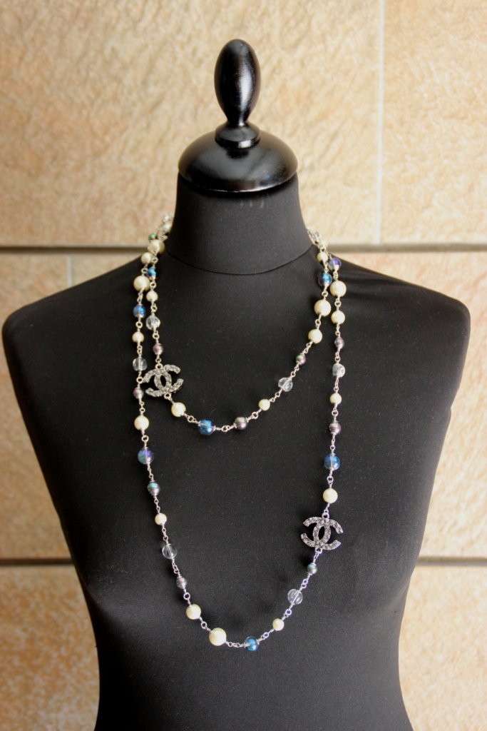 CHANEL Sautoir composé d'une chaînette, de perles: CHANEL Sautoir composé d'une chaînette, de perles blanches, transparentes et bleues et de sigles de la marque. Bon état.