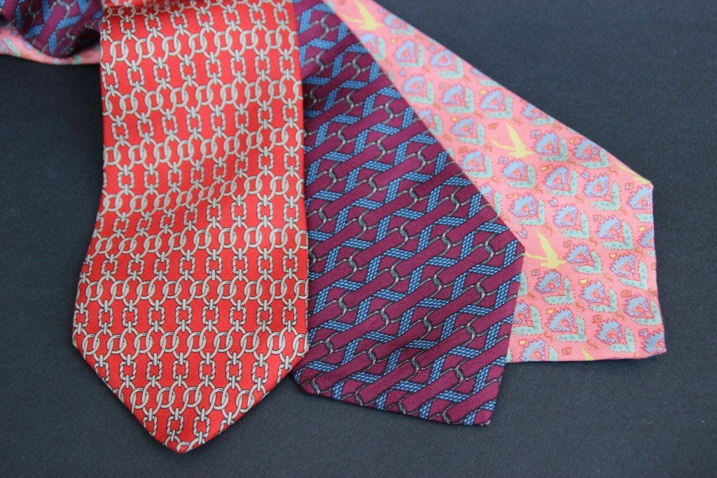 HERMES Lot de trois cravates en soie imprimée dans des: HERMES Lot de trois cravates en soie imprimée dans des tons de rouge, bordeaux et saumon. Bon état.