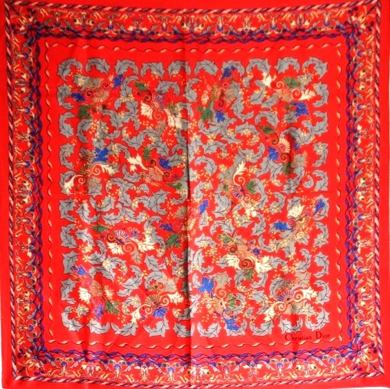CHRISTIAN DIOR Carré en soie rouge vif à décor: CHRISTIAN DIOR Carré en soie rouge vif à décor ornemental végétal gris, vert, écru et bleu roi. Vers 1980 Bon état