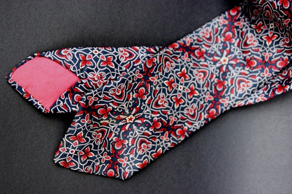 CHRISTIAN DIOR - Paris Made in France Cravate en soie: CHRISTIAN DIOR - Paris Made in France Cravate en soie bleu marine à décor d'arabesques grises et rouges. Bon état.