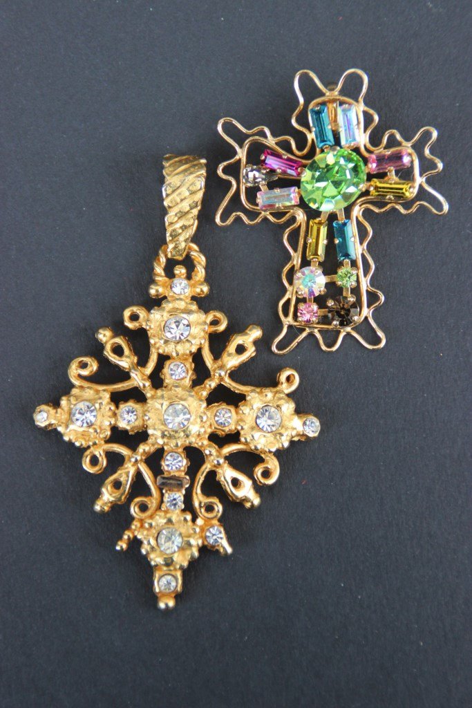 CHRISTIAN LACROIX Lot composé de deux broches/: CHRISTIAN LACROIX Lot composé de deux broches/ Pendentifs en forme de croix, En métal doré et strass : une Blanche et une polychrome. Etat d'usage (manque un strass Sur la plus grande croix)